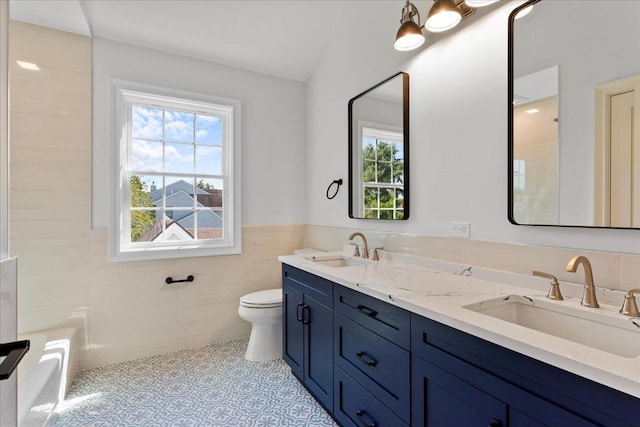 bathroom with vanity, toilet, tile walls, and a wealth of natural light