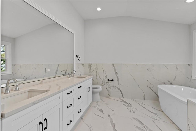 bathroom with vanity, vaulted ceiling, toilet, a tub to relax in, and tile walls