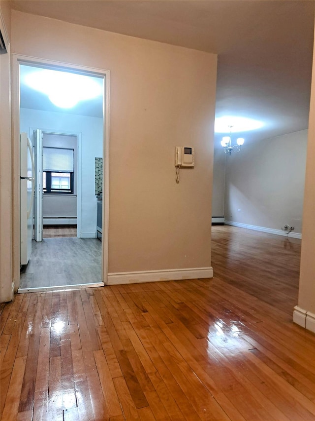 corridor with wood-type flooring, a baseboard heating unit, and a notable chandelier