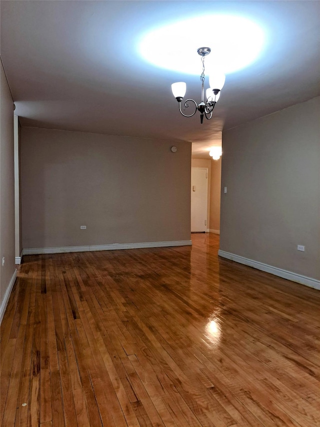 spare room with wood-type flooring and an inviting chandelier