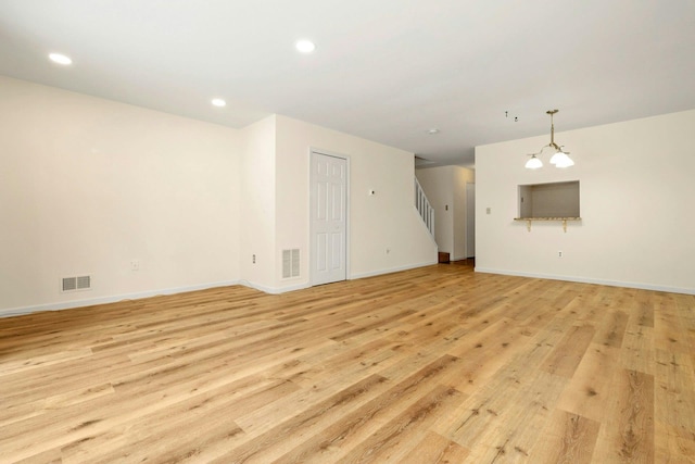 unfurnished living room with an inviting chandelier and light hardwood / wood-style flooring