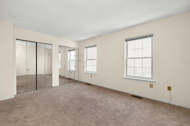 unfurnished bedroom featuring light colored carpet and two closets