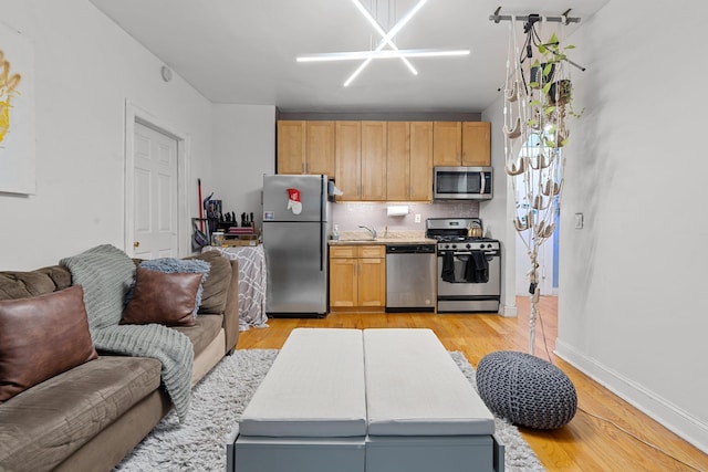 kitchen with light brown cabinets, backsplash, sink, appliances with stainless steel finishes, and light hardwood / wood-style floors