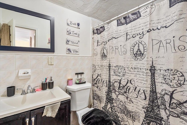 bathroom with a textured ceiling, vanity, tile walls, and toilet