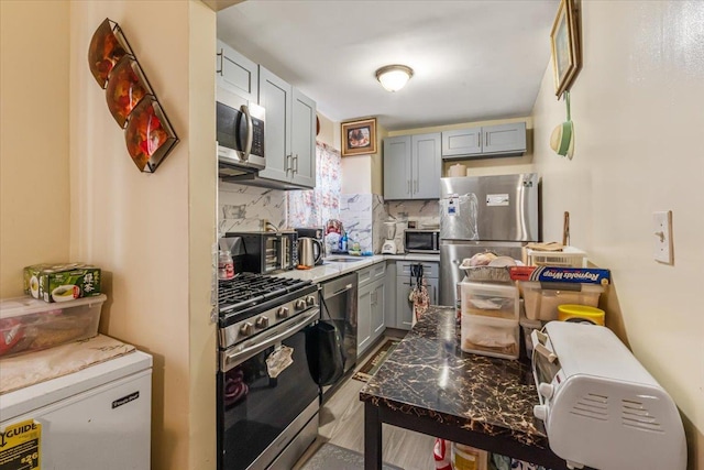 kitchen featuring sink, stainless steel appliances, backsplash, gray cabinets, and light wood-type flooring