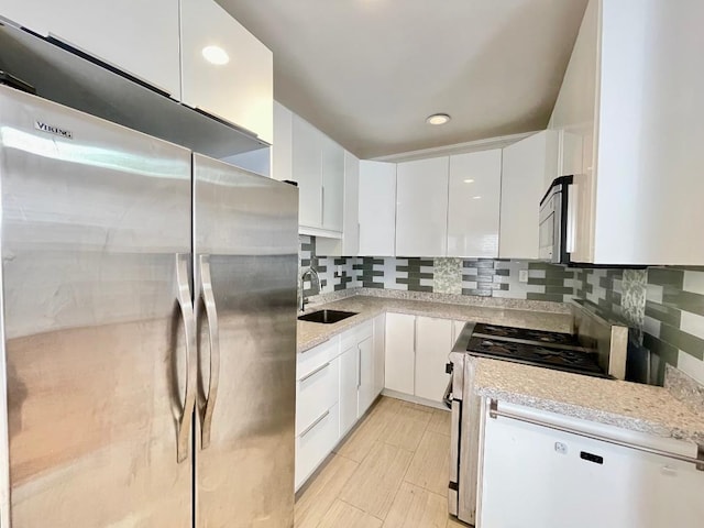 kitchen featuring backsplash, sink, appliances with stainless steel finishes, light stone counters, and white cabinetry