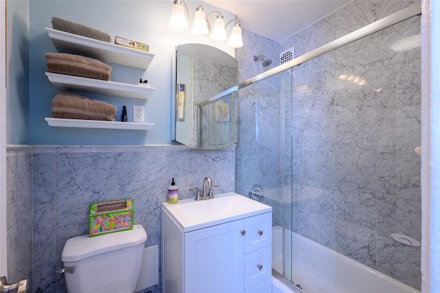 full bathroom featuring shower / bath combination with glass door, vanity, toilet, and tile walls