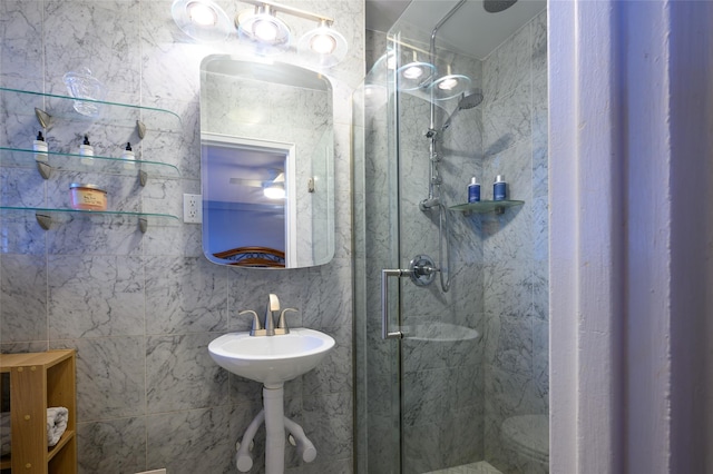 bathroom with sink, a shower with shower door, and tile walls