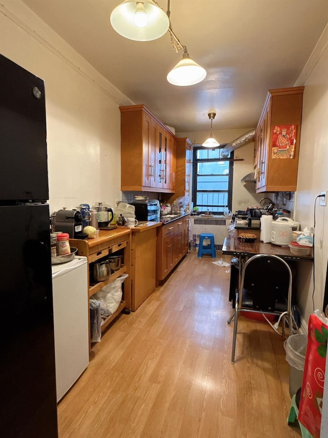 kitchen with black refrigerator, light wood-type flooring, radiator, crown molding, and hanging light fixtures