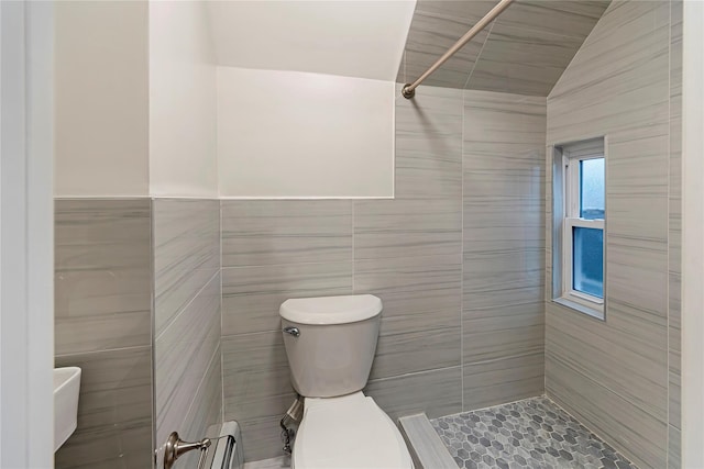 bathroom with tiled shower, vaulted ceiling, toilet, and tile walls