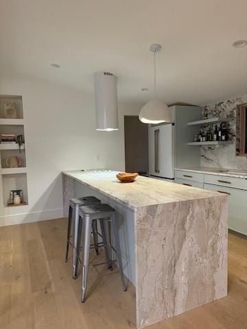 kitchen featuring white cabinetry, light hardwood / wood-style floors, decorative light fixtures, a kitchen breakfast bar, and built in shelves