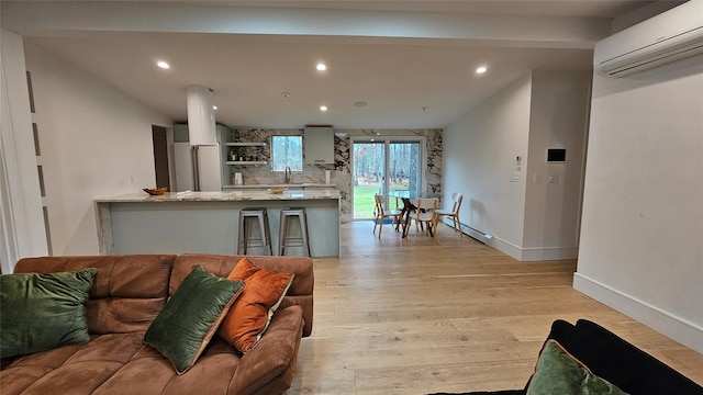 living room with light wood-type flooring, baseboard heating, a wall mounted AC, and sink