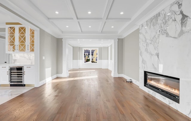 unfurnished living room featuring coffered ceiling, beverage cooler, indoor bar, a fireplace, and light hardwood / wood-style floors