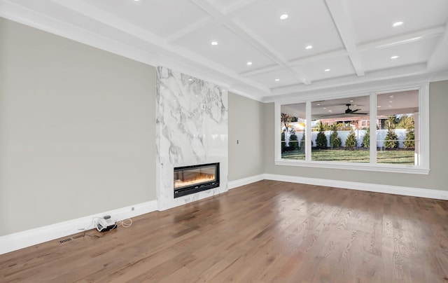 unfurnished living room with coffered ceiling, ceiling fan, beam ceiling, a fireplace, and hardwood / wood-style floors