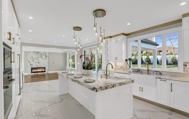 kitchen featuring white cabinets, a center island with sink, hanging light fixtures, and sink