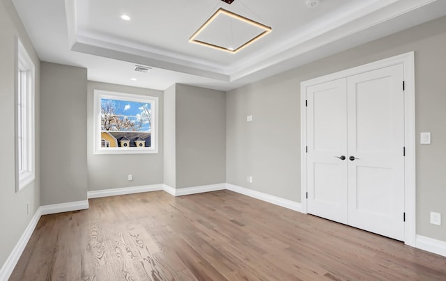 unfurnished bedroom with light hardwood / wood-style floors and a raised ceiling