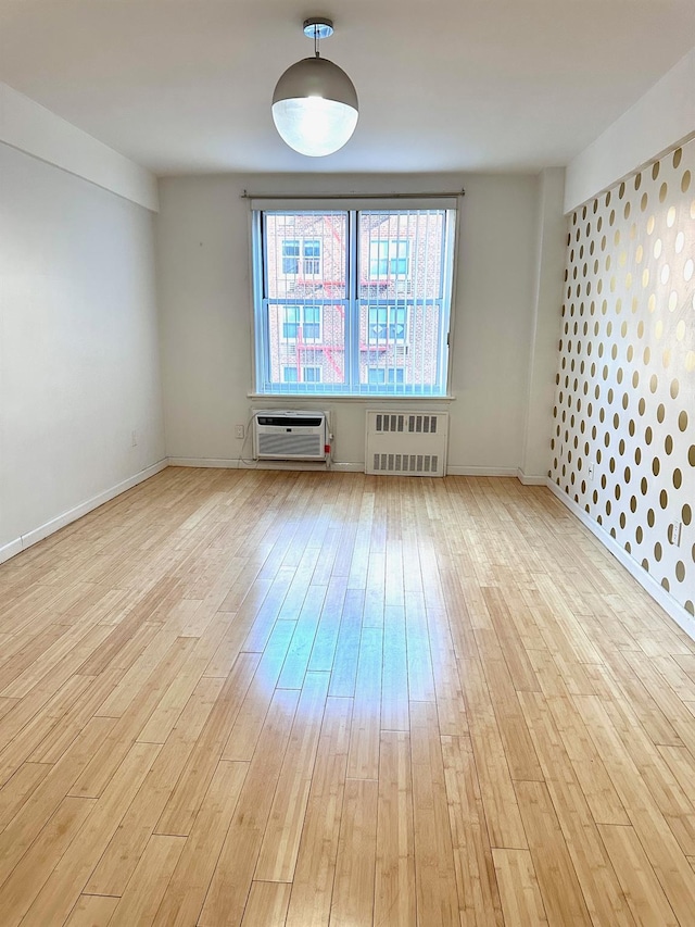 spare room with a wall unit AC, radiator, and light hardwood / wood-style floors