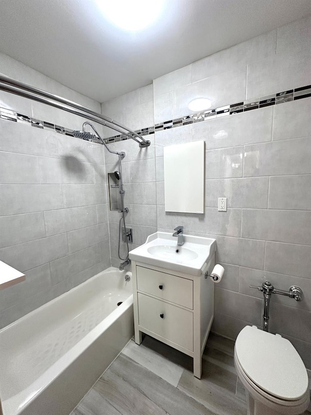 full bathroom featuring tiled shower / bath combo, hardwood / wood-style floors, toilet, vanity, and tile walls