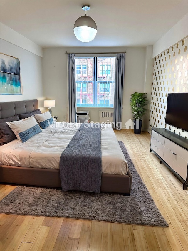 bedroom with radiator heating unit, light wood-type flooring, and a wall mounted AC