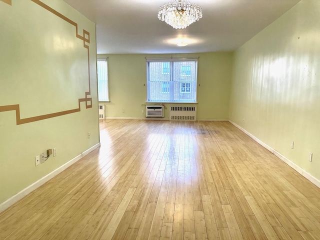 spare room featuring an inviting chandelier, radiator heating unit, a wall unit AC, and light hardwood / wood-style flooring