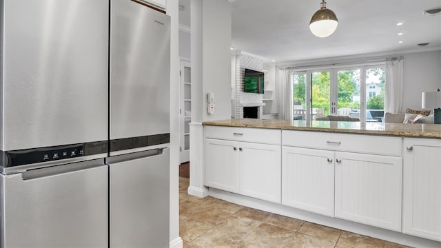 kitchen with white cabinetry, stainless steel fridge, hanging light fixtures, crown molding, and light stone counters