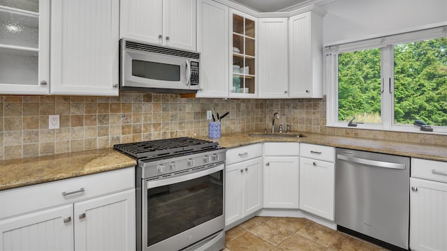 kitchen with light tile patterned flooring, sink, white cabinetry, stainless steel appliances, and light stone counters