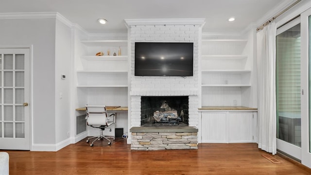 living room featuring built in desk, a fireplace, ornamental molding, and hardwood / wood-style floors