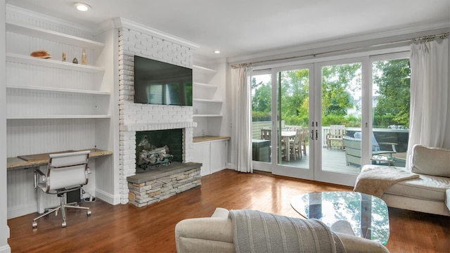 living room with a brick fireplace, wood-type flooring, crown molding, built in shelves, and french doors