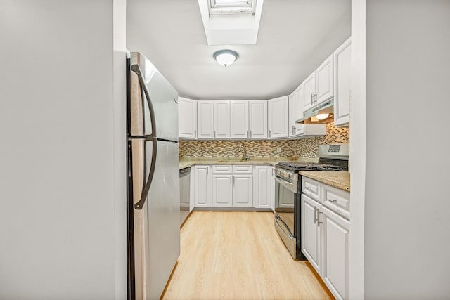 kitchen with light wood-type flooring, a skylight, backsplash, stainless steel appliances, and white cabinets