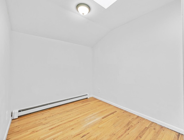 empty room featuring hardwood / wood-style floors, vaulted ceiling, and a baseboard radiator