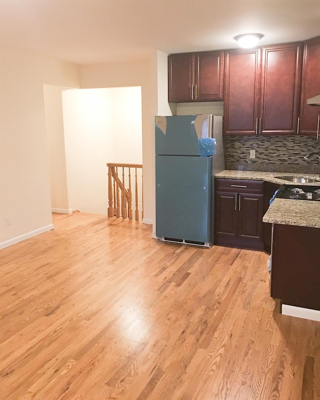 kitchen with sink, tasteful backsplash, light stone counters, stainless steel fridge, and light hardwood / wood-style floors