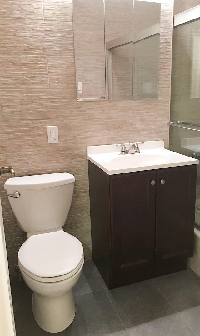 bathroom with vanity, a shower with door, tile patterned flooring, toilet, and tile walls