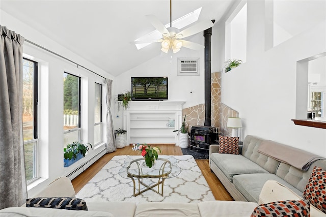 living room featuring a wood stove, ceiling fan, baseboard heating, light hardwood / wood-style flooring, and lofted ceiling with skylight