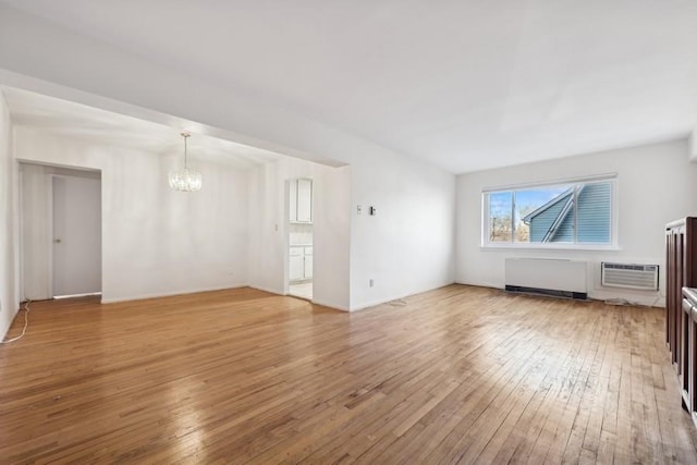 unfurnished living room featuring hardwood / wood-style flooring, an AC wall unit, radiator, and a notable chandelier