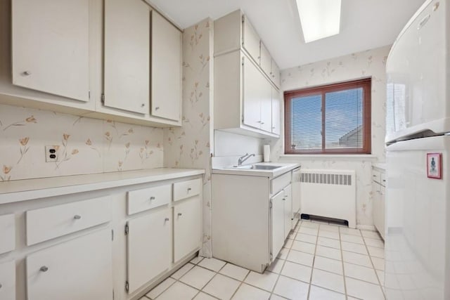 kitchen featuring sink, white cabinetry, light tile patterned floors, and radiator