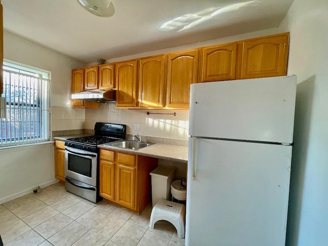 kitchen with white refrigerator, sink, stainless steel gas range, light tile patterned floors, and tasteful backsplash