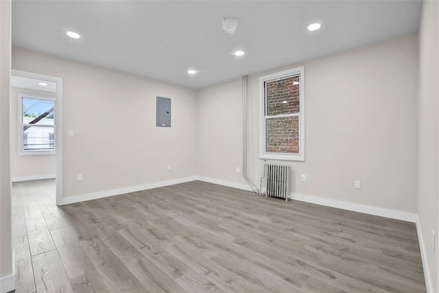 spare room featuring electric panel, light wood-type flooring, and radiator