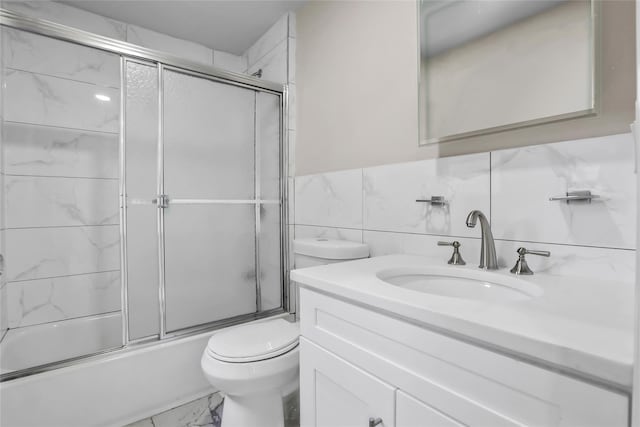 full bathroom with vanity, bath / shower combo with glass door, tile walls, and toilet