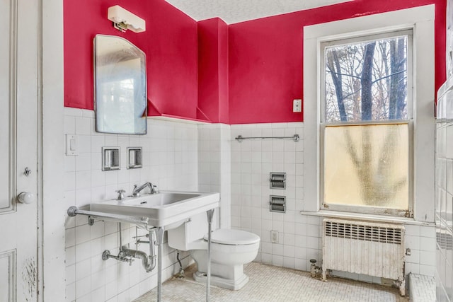 bathroom featuring radiator, sink, tile patterned floors, toilet, and tile walls