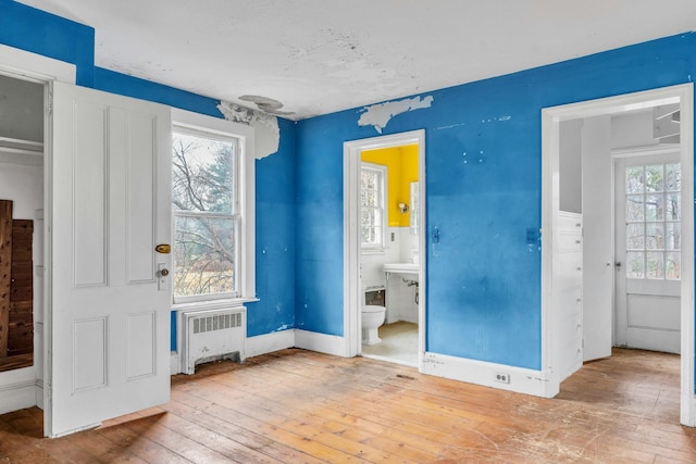 unfurnished bedroom featuring light hardwood / wood-style flooring, radiator, and connected bathroom