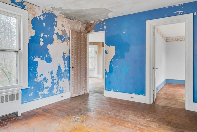 empty room featuring wood-type flooring, radiator heating unit, and a wealth of natural light