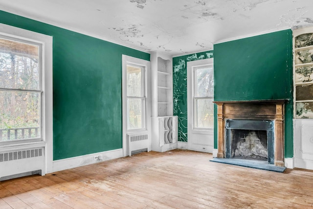 unfurnished living room with a healthy amount of sunlight, radiator heating unit, and hardwood / wood-style floors