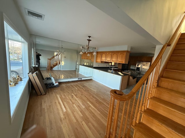 kitchen featuring stainless steel fridge, decorative light fixtures, light hardwood / wood-style floors, and kitchen peninsula