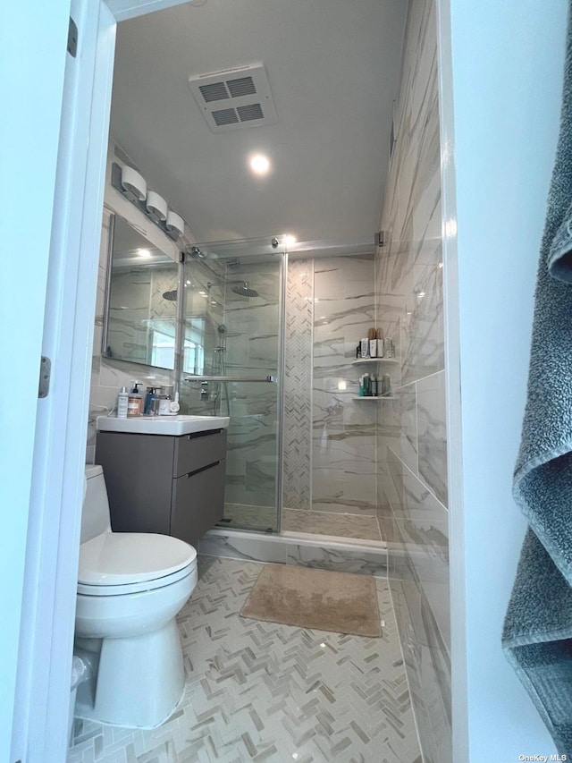 bathroom featuring vanity, toilet, a shower with door, and tile walls