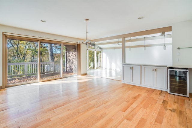 unfurnished dining area with wine cooler, an inviting chandelier, and light wood-type flooring