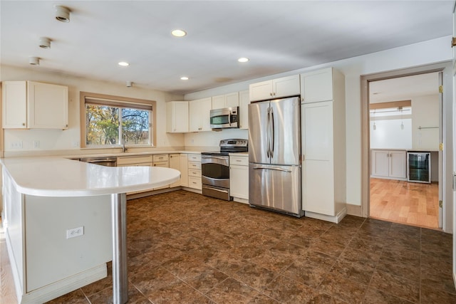 kitchen featuring kitchen peninsula, a breakfast bar, stainless steel appliances, white cabinetry, and wine cooler