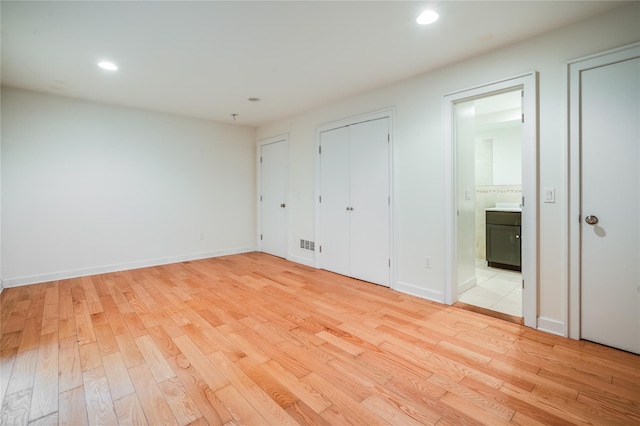 unfurnished bedroom featuring ensuite bathroom, light hardwood / wood-style flooring, and two closets