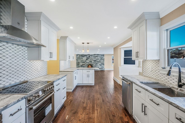 kitchen with backsplash, stainless steel appliances, sink, wall chimney range hood, and decorative light fixtures