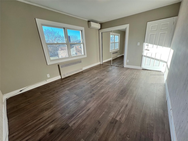 empty room featuring a wall mounted AC, radiator, and dark wood-type flooring