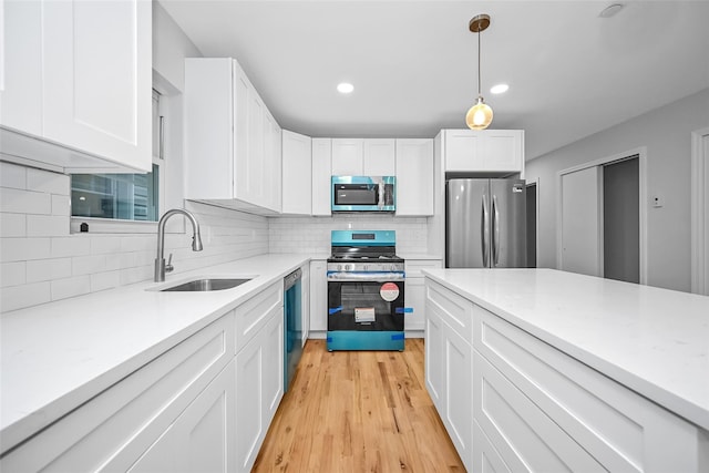 kitchen with white cabinets, sink, hanging light fixtures, light hardwood / wood-style floors, and stainless steel appliances